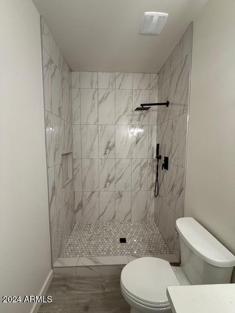 bathroom with a tile shower, vanity, and toilet