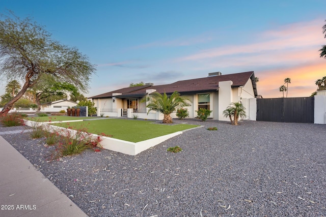 ranch-style home featuring a front yard, a gate, a garage, fence, and stucco siding