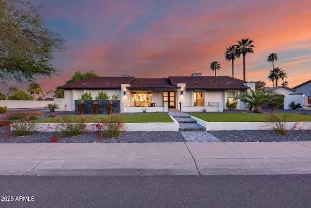ranch-style home featuring a lawn, fence private yard, a porch, and stucco siding