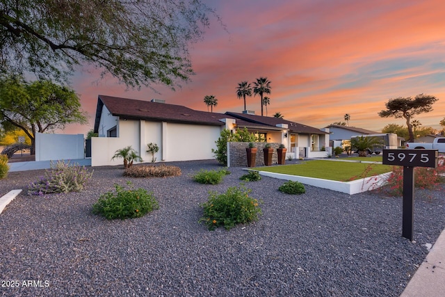 view of front facade featuring fence, stucco siding, and a lawn
