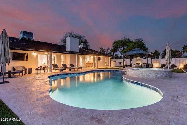 pool at dusk featuring fence, a gazebo, a pool with connected hot tub, central AC unit, and a patio