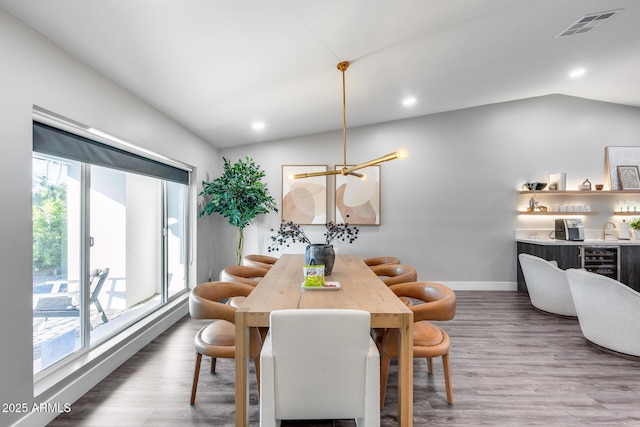 dining room with baseboards, visible vents, wood finished floors, and vaulted ceiling