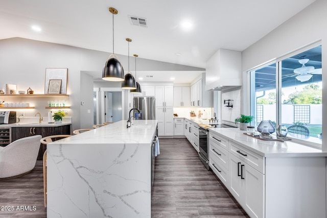 kitchen featuring appliances with stainless steel finishes, a sink, white cabinetry, lofted ceiling, and visible vents