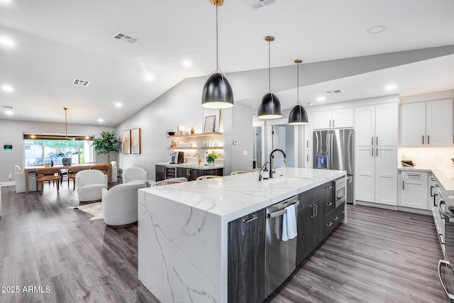 kitchen featuring visible vents, an island with sink, a sink, vaulted ceiling, and stainless steel appliances