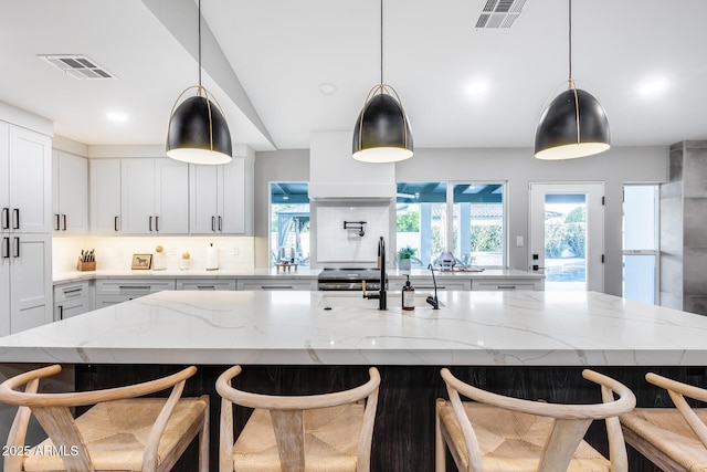 kitchen featuring white cabinets, visible vents, decorative backsplash, and light stone counters