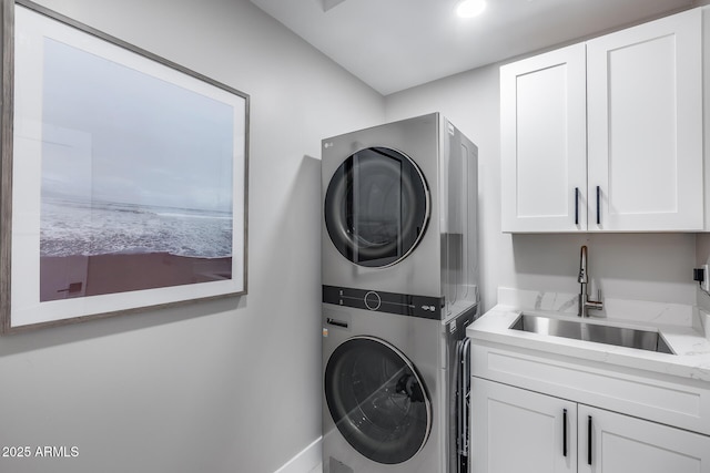 clothes washing area with a sink, cabinet space, and stacked washing maching and dryer