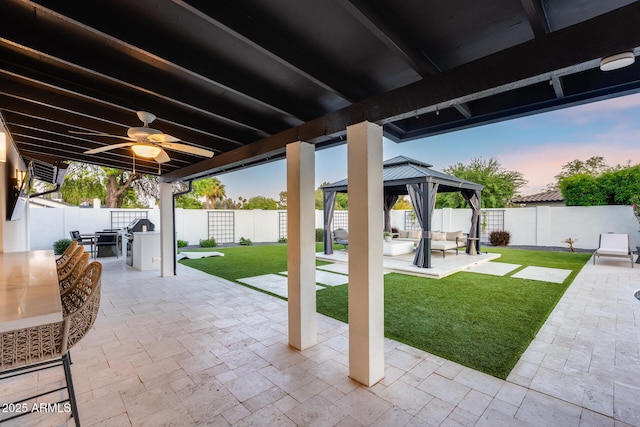 patio terrace at dusk featuring a fenced backyard, an outdoor hangout area, a gazebo, and a yard