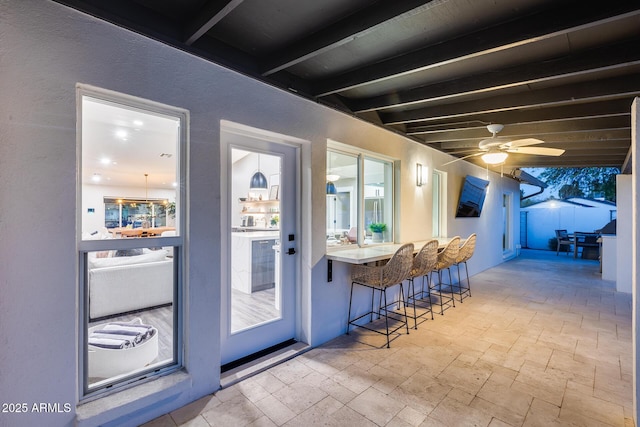 bar with ceiling fan, beamed ceiling, and stone tile floors