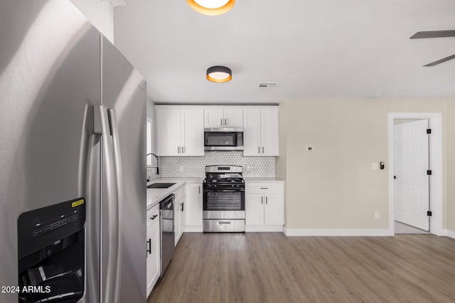 kitchen with decorative backsplash, appliances with stainless steel finishes, sink, white cabinets, and light hardwood / wood-style floors