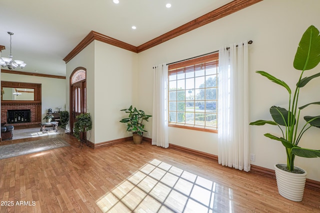 entryway featuring light wood-style floors, ornamental molding, a brick fireplace, a chandelier, and baseboards