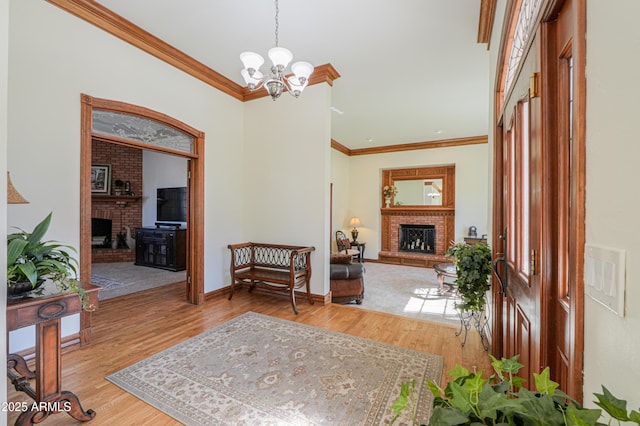 foyer entrance with a notable chandelier, a fireplace, light wood-style floors, ornamental molding, and baseboards