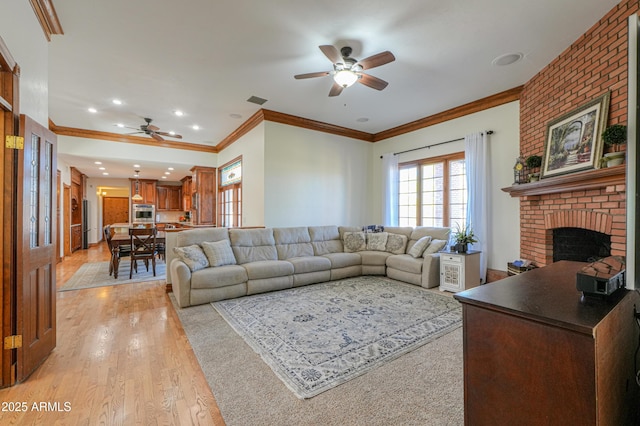 living area with visible vents, a ceiling fan, crown molding, light wood-style floors, and a fireplace