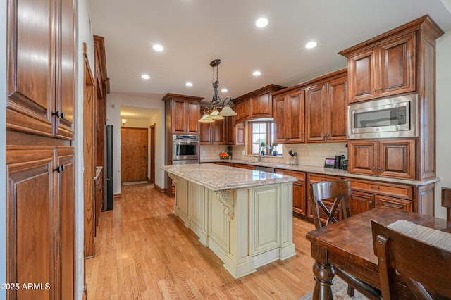 kitchen with brown cabinetry, a kitchen island, decorative light fixtures, light stone countertops, and stainless steel appliances