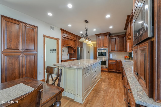 kitchen with hanging light fixtures, appliances with stainless steel finishes, white cabinets, a kitchen island, and light stone countertops