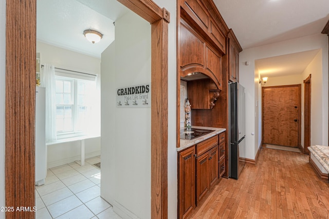 interior space featuring freestanding refrigerator, light wood-style flooring, baseboards, and black electric cooktop