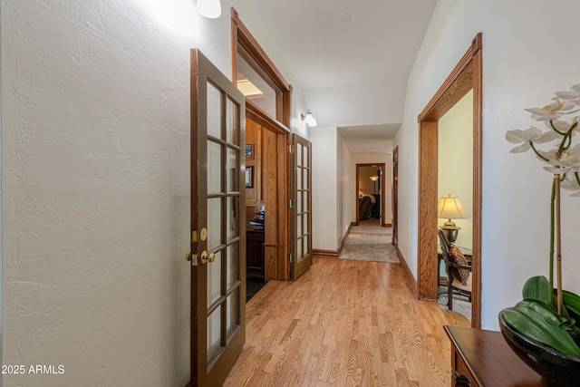 corridor featuring light wood-style floors, baseboards, and a textured wall