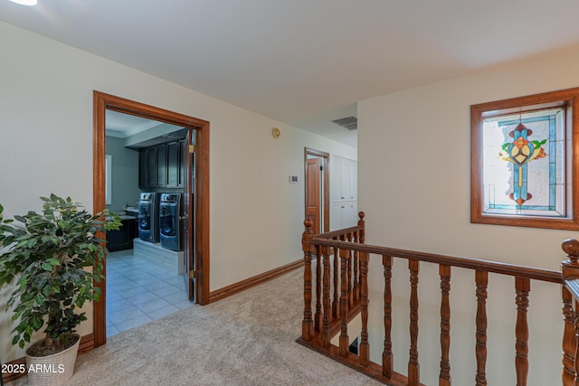 hall featuring light colored carpet, visible vents, baseboards, an upstairs landing, and washer and dryer