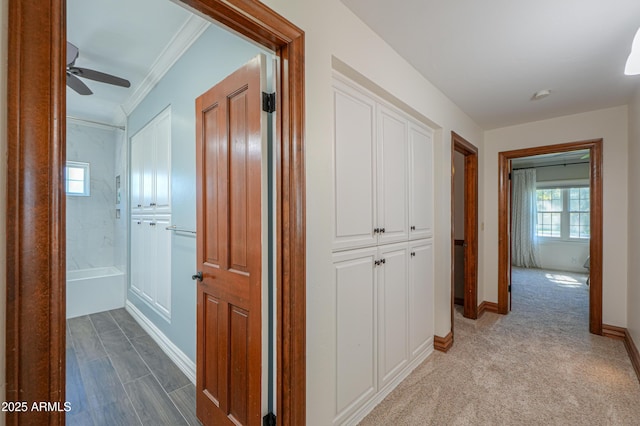 hall with ornamental molding, light colored carpet, and baseboards