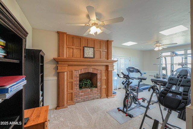 workout area with light carpet, ceiling fan, wainscoting, and a brick fireplace