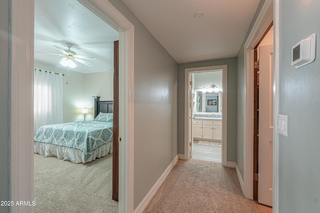 hall featuring baseboards, a sink, and light colored carpet