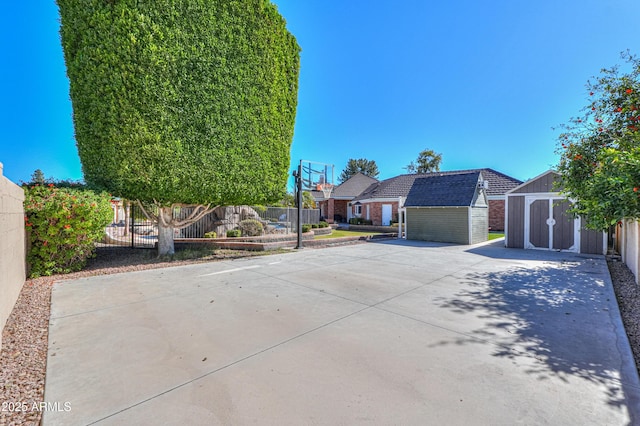 exterior space featuring driveway, fence, a storage unit, an outdoor structure, and brick siding