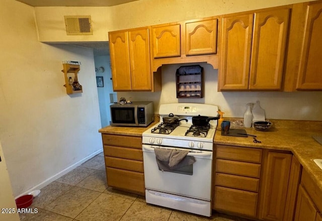 kitchen featuring visible vents, baseboards, stainless steel microwave, brown cabinets, and white gas range