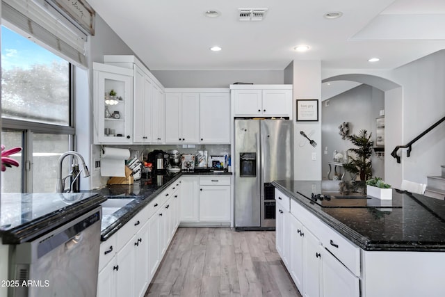 kitchen featuring arched walkways, a sink, visible vents, appliances with stainless steel finishes, and dark stone counters