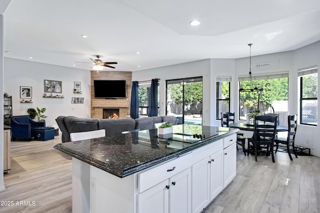 kitchen with recessed lighting, a fireplace, white cabinetry, light wood-style floors, and dark stone countertops