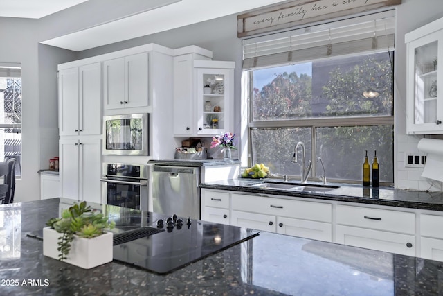 kitchen with a sink, white cabinetry, appliances with stainless steel finishes, decorative backsplash, and dark stone countertops