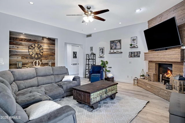 living room featuring baseboards, light wood-style flooring, ceiling fan, a fireplace, and recessed lighting