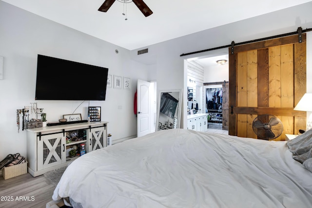 bedroom with a walk in closet, visible vents, a barn door, a ceiling fan, and light wood-type flooring