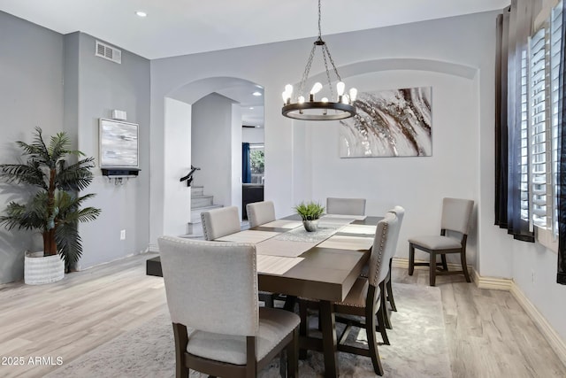 dining room with light wood finished floors, baseboards, visible vents, stairs, and a notable chandelier