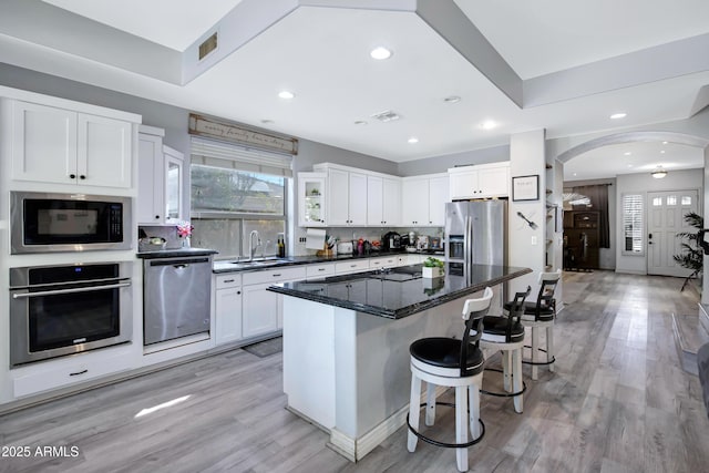 kitchen with arched walkways, appliances with stainless steel finishes, a breakfast bar area, and a wealth of natural light