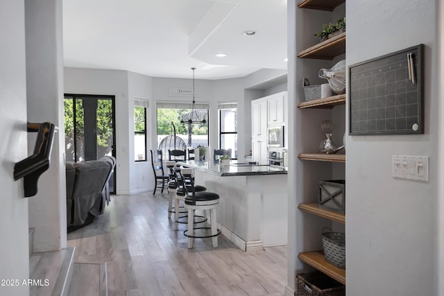 kitchen with light wood finished floors, open shelves, stainless steel appliances, white cabinets, and a kitchen bar