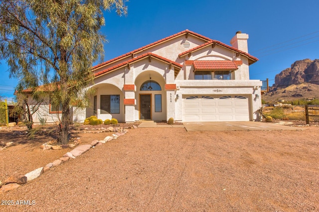 mediterranean / spanish-style home featuring a garage, a tile roof, driveway, stucco siding, and a chimney