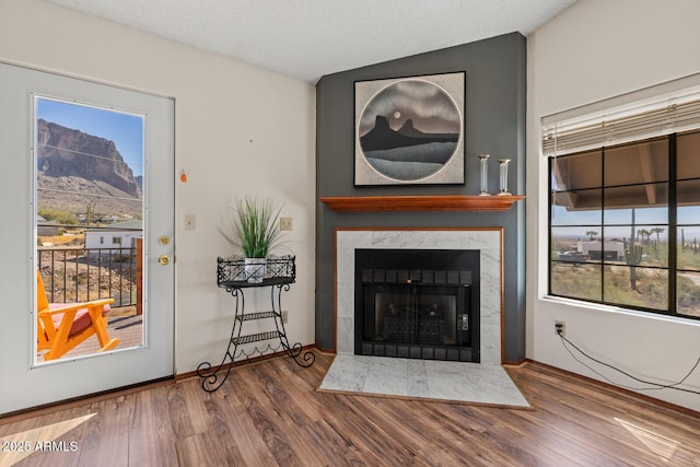 living area featuring baseboards, a textured ceiling, a tiled fireplace, and wood finished floors