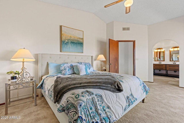 bedroom featuring carpet floors, arched walkways, lofted ceiling, visible vents, and ensuite bathroom