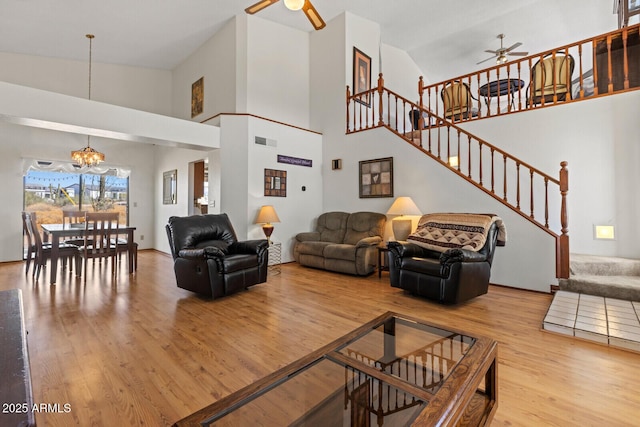 living room featuring ceiling fan with notable chandelier, wood finished floors, stairs, and visible vents