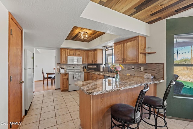 kitchen with a peninsula, white appliances, tasteful backsplash, and a tray ceiling