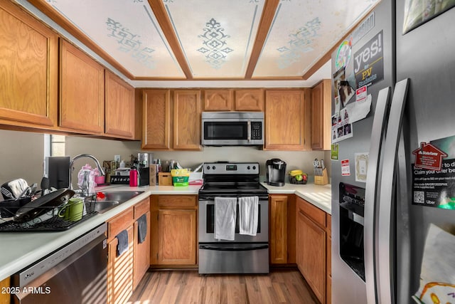 kitchen featuring light countertops, a sink, light wood-type flooring, brown cabinetry, and appliances with stainless steel finishes