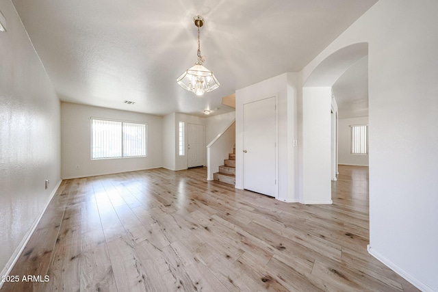 spare room with arched walkways, stairway, visible vents, and light wood-style floors