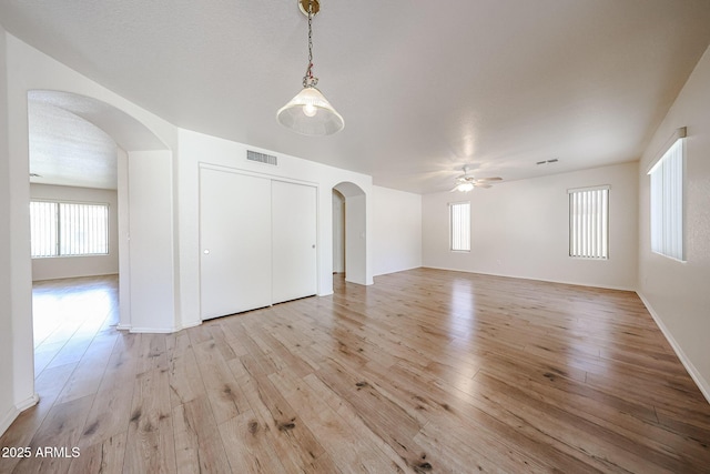 unfurnished room with arched walkways, visible vents, ceiling fan, and light wood-style flooring