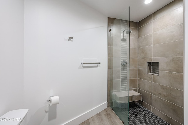 bathroom featuring toilet, a tile shower, and wood-type flooring