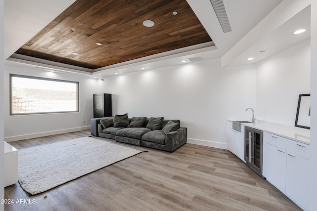 living room with light wood-type flooring, indoor wet bar, wood ceiling, a tray ceiling, and beverage cooler