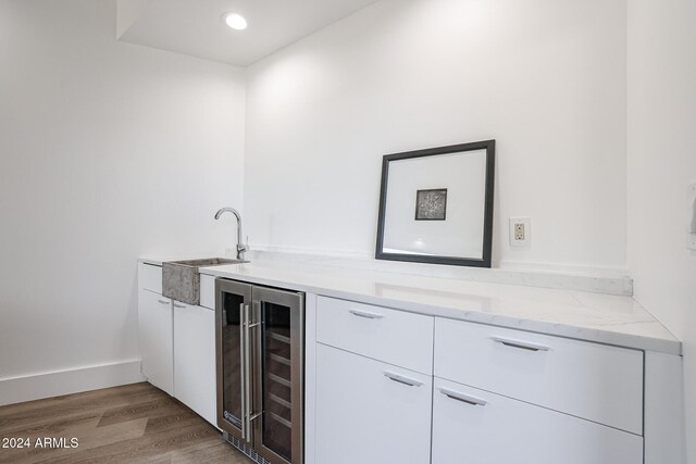 bar with beverage cooler, light stone counters, white cabinetry, light hardwood / wood-style floors, and sink