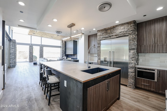 kitchen featuring a kitchen island with sink, decorative light fixtures, light wood-type flooring, appliances with stainless steel finishes, and tasteful backsplash