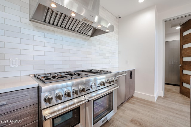 kitchen with wall chimney exhaust hood, tasteful backsplash, range with two ovens, and light wood-type flooring