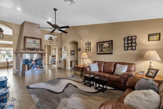 tiled living room with a towering ceiling, ceiling fan with notable chandelier, and a fireplace