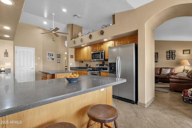 kitchen featuring a breakfast bar, kitchen peninsula, a kitchen island, ceiling fan, and stainless steel appliances