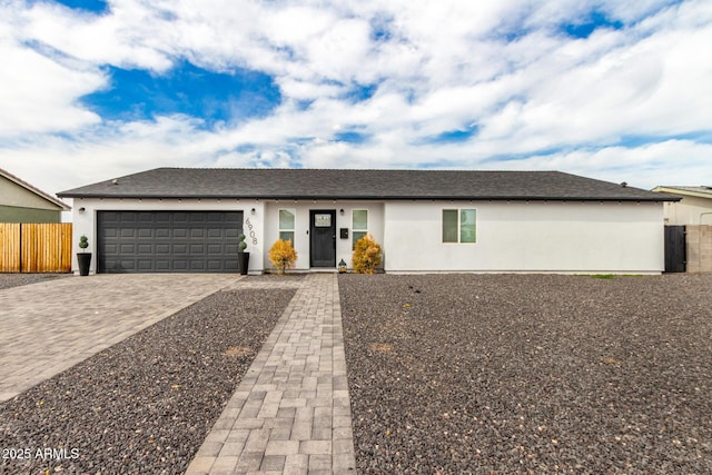 ranch-style house featuring decorative driveway, stucco siding, fence, and an attached garage